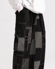Black patchwork cargo pants in three-quarter view, with the large flap pocket on the outer leg