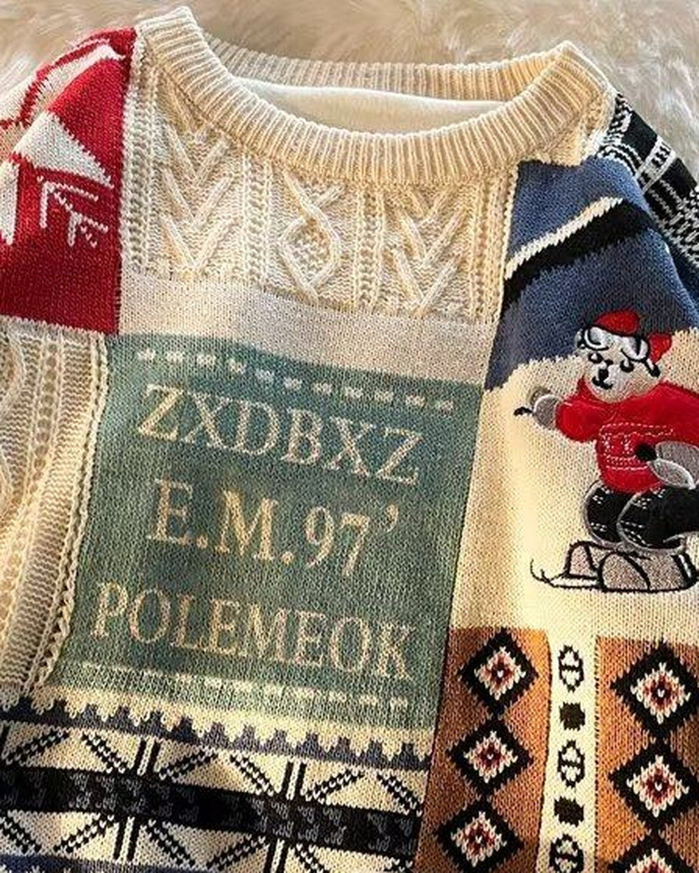 Close-up of the lettered patch and jacquard bands on the cream patchwork sweater