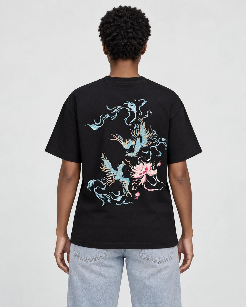Model wearing the black phoenix and lotus print T-shirt with light-wash jeans, back view