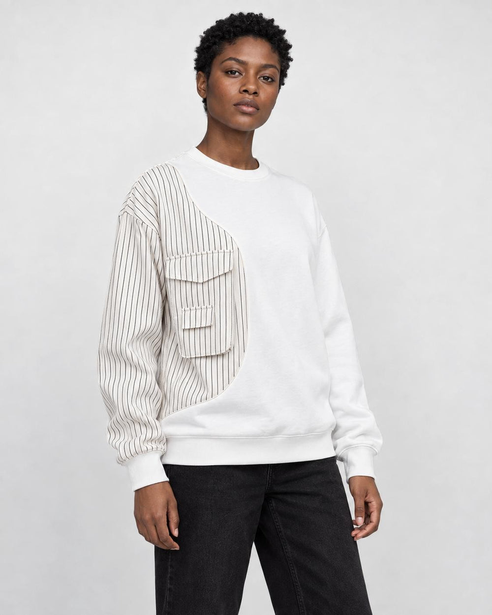 Model wearing the white pinstripe panel crewneck sweatshirt with black jeans, three-quarter view