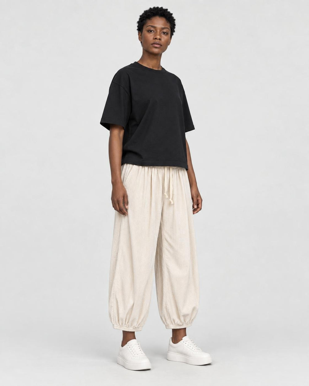 Model wearing the cream pleated corduroy pants with a black tee, three-quarter view
