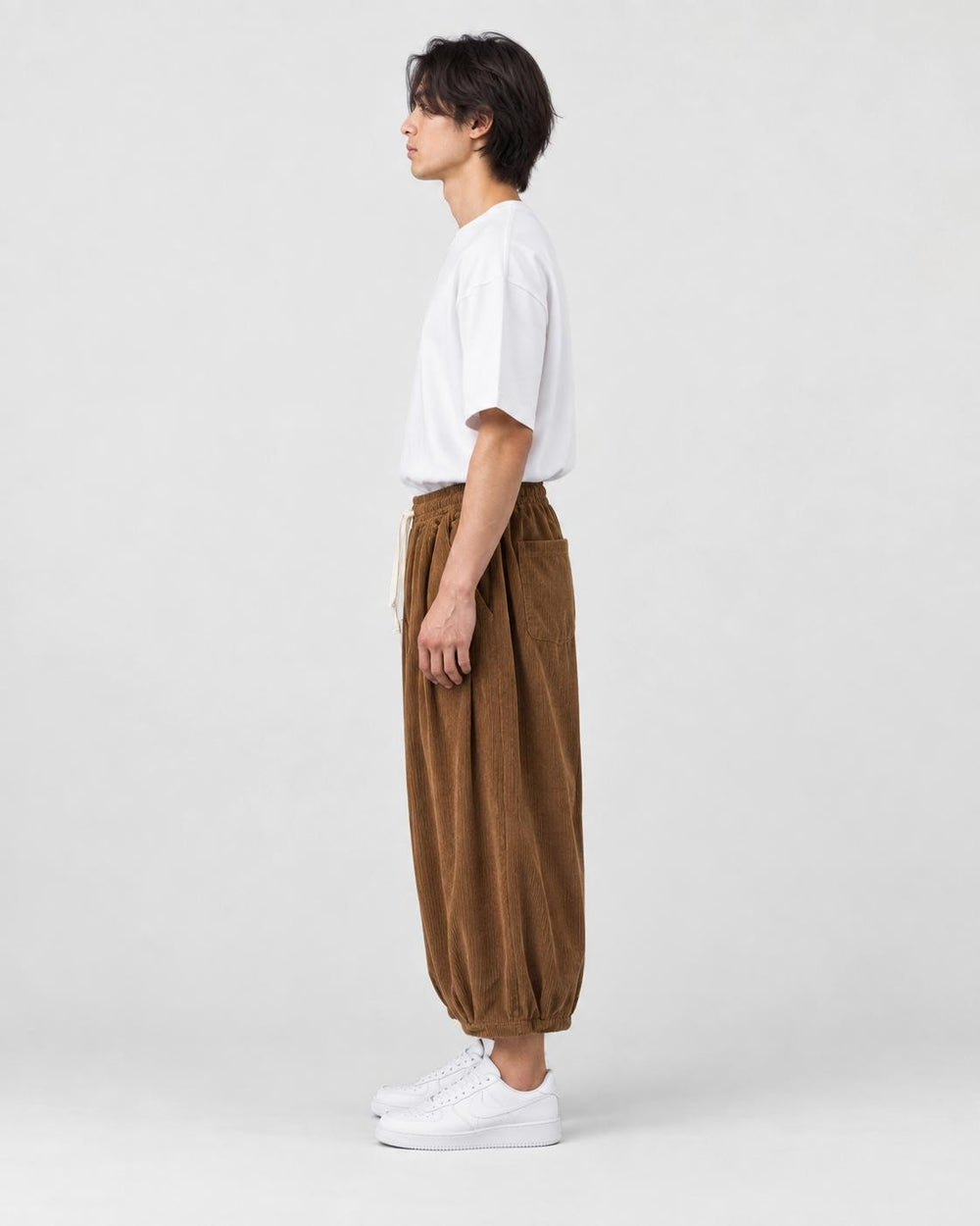 Model wearing the brown corduroy wide-leg pants, side view of the gathered hem