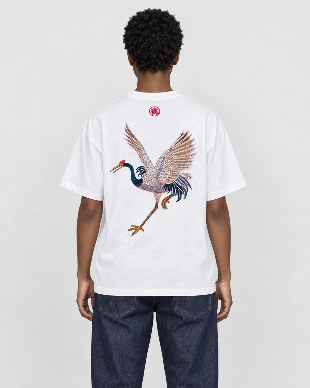 Model wearing the white crane embroidered T-shirt with dark jeans, back view