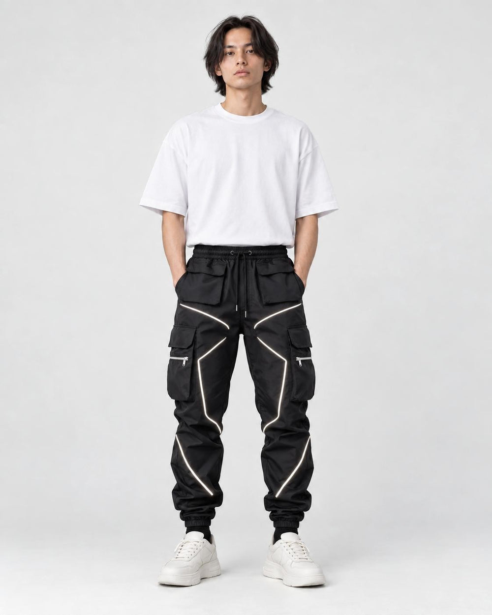 Model wearing black cargo joggers with silver reflective tape lines, a white tee and chunky sneakers, front view