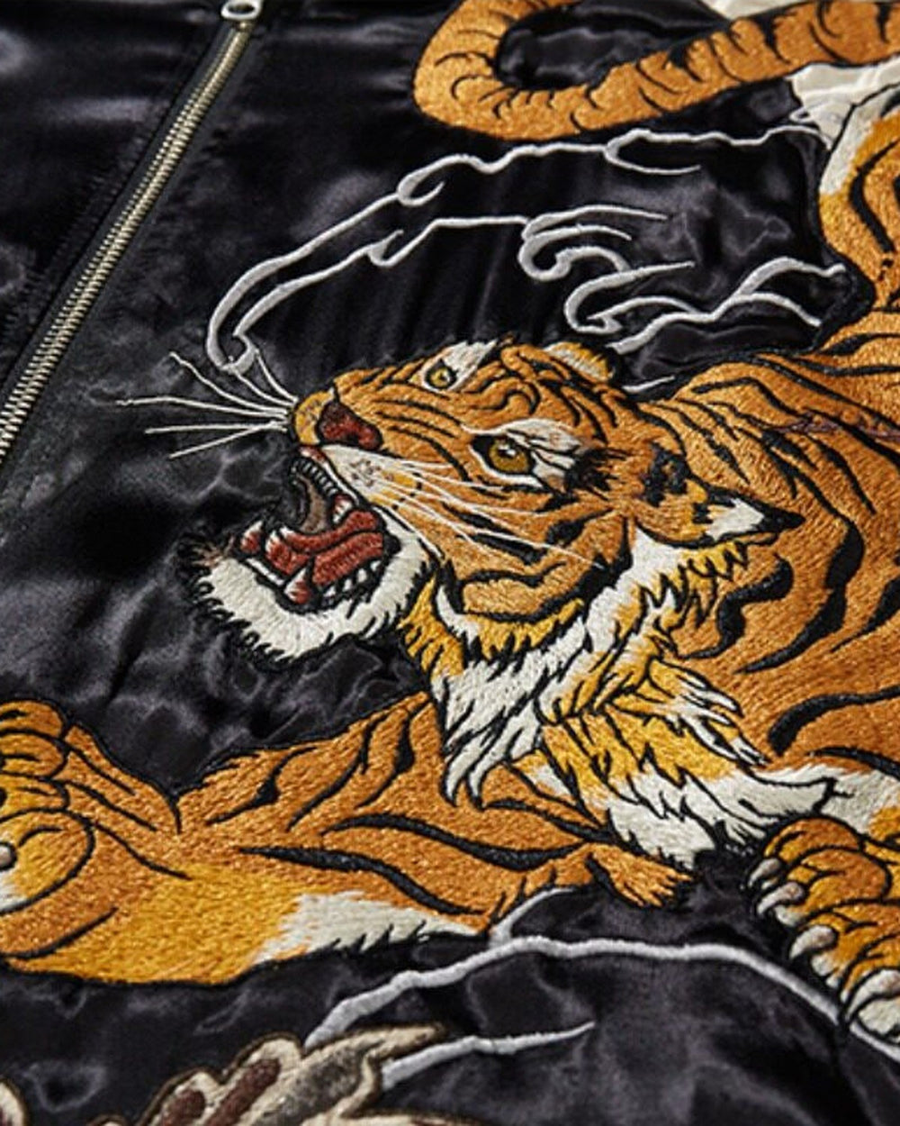 Close view of the orange and gold tiger embroidery with white whiskers beside the zip on glossy black fabric
