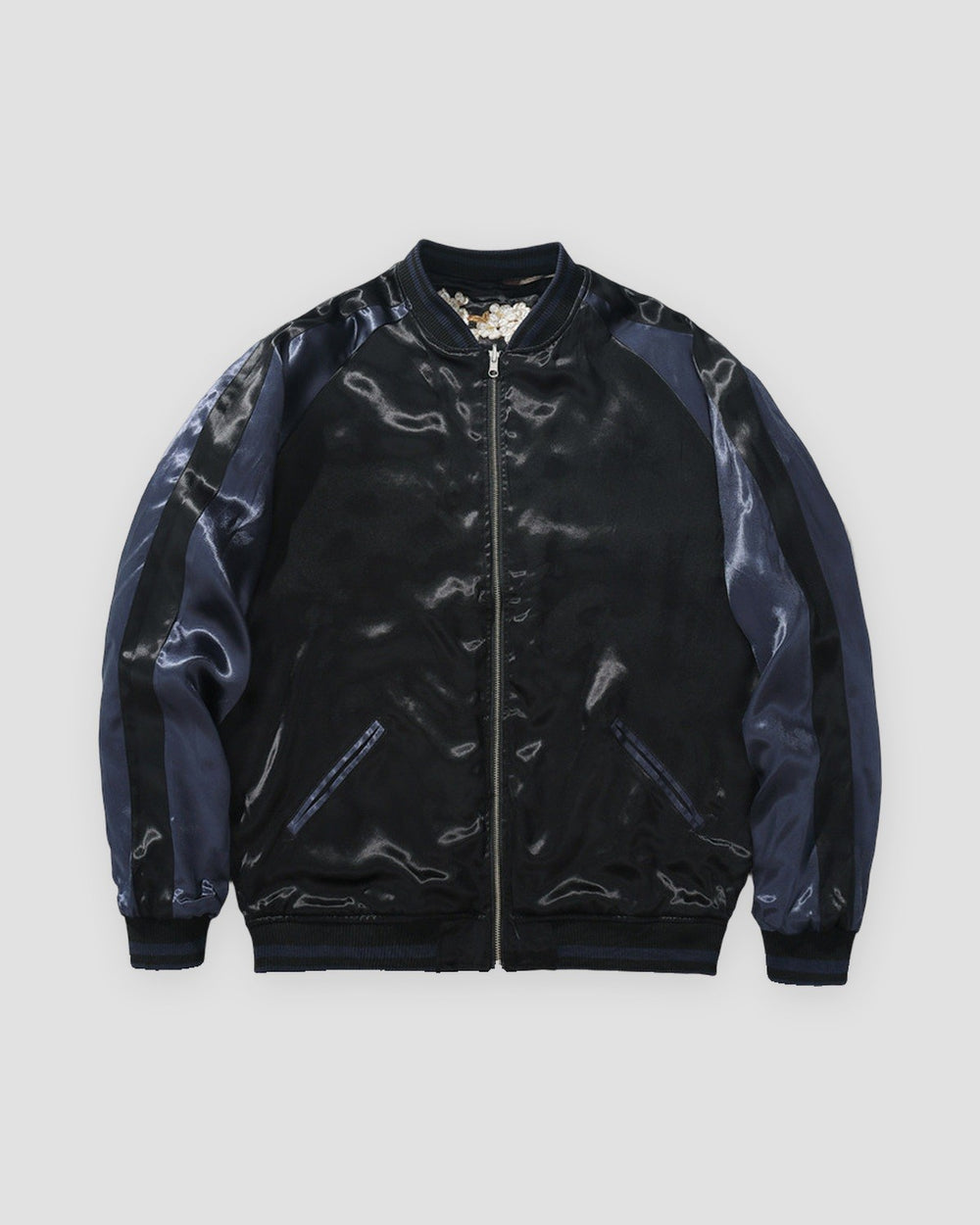 Plain reverse side of the jacket in glossy black with navy raglan sleeves and a silver zip