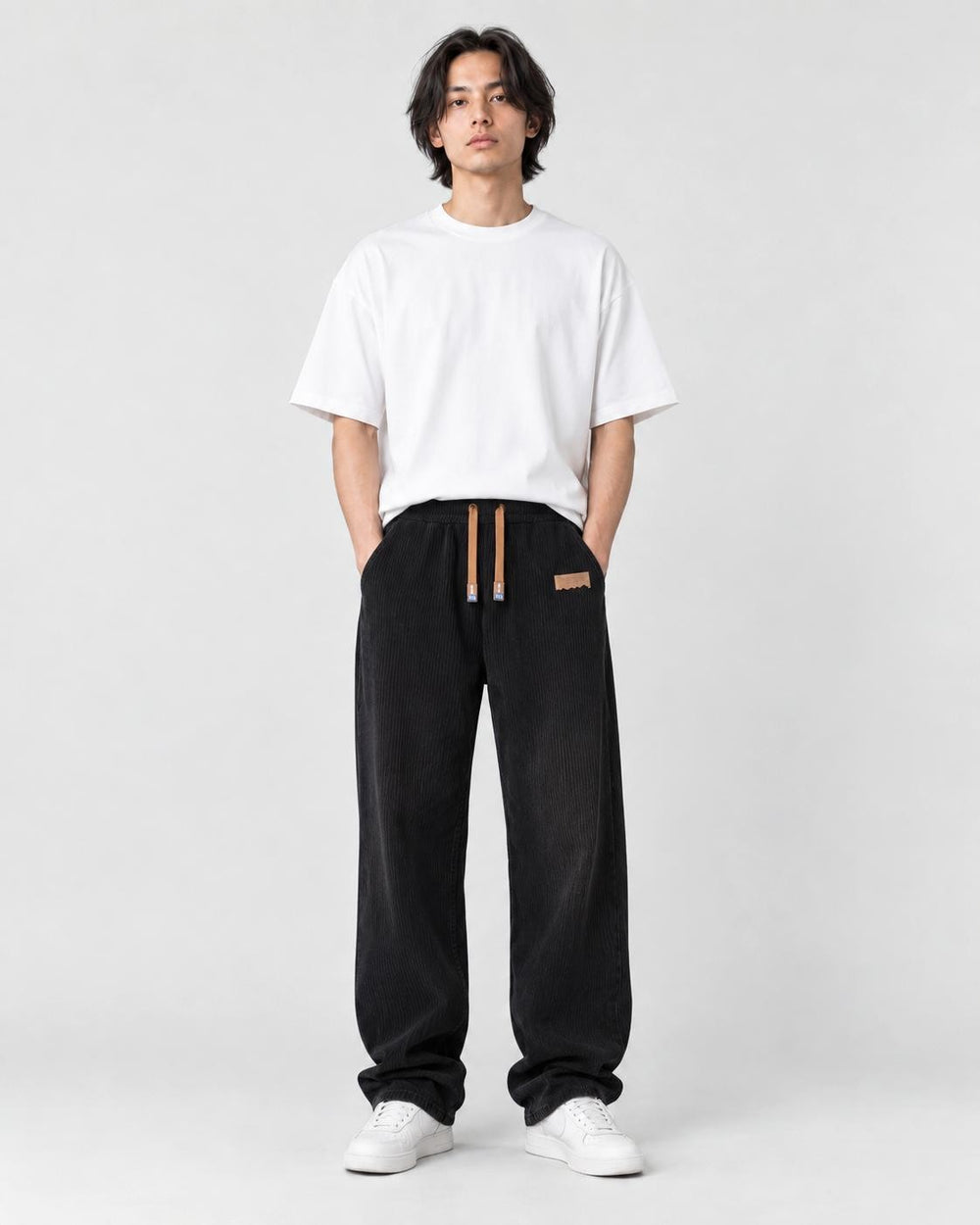 Model wearing black ribbed corduroy wide-leg pants with a white tee and white sneakers, front view