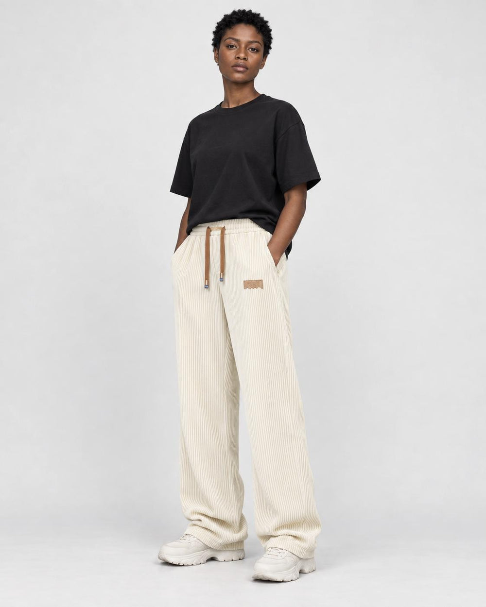 Model wearing cream ribbed corduroy wide-leg pants with a black tee and white sneakers, three-quarter view