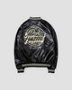 Black bomber jacket with a large round cream script badge on the back, back view