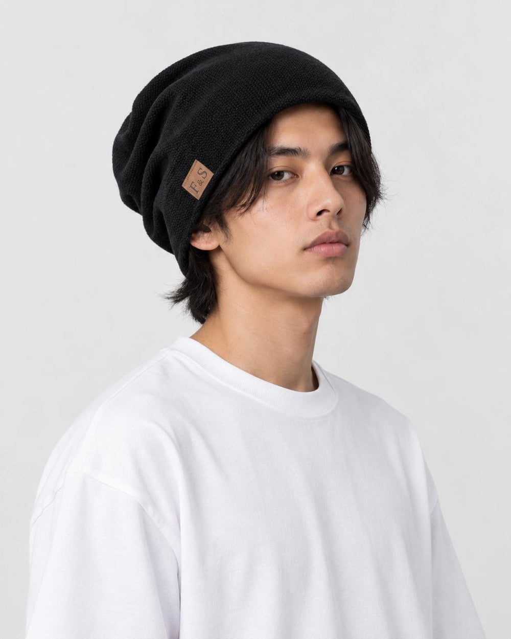 Model wearing the black slouch beanie low over the ears with a white tee, three-quarter view
