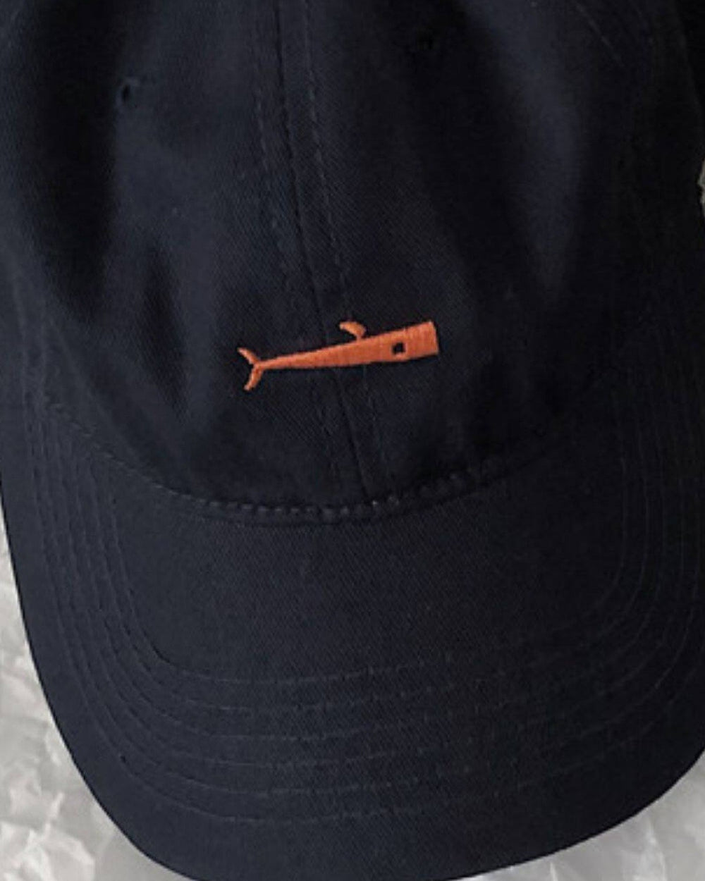 Close-up of the small orange whale embroidered on the navy cap