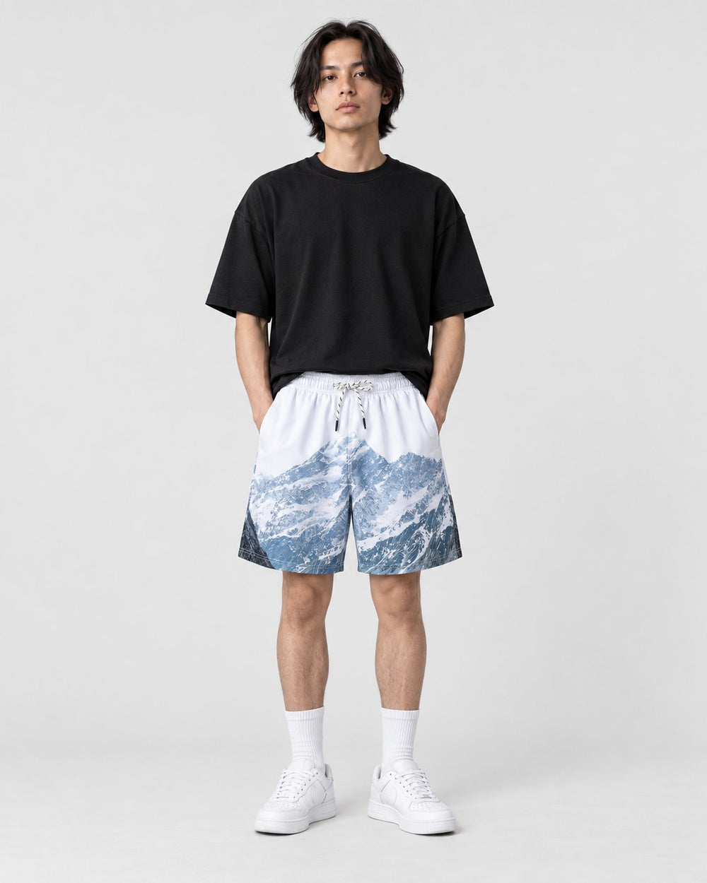 Model wearing the snowy mountain print shorts with a black T-shirt, front view