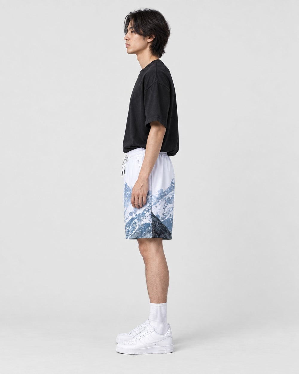 Model wearing the snowy mountain print shorts with a black T-shirt, side view