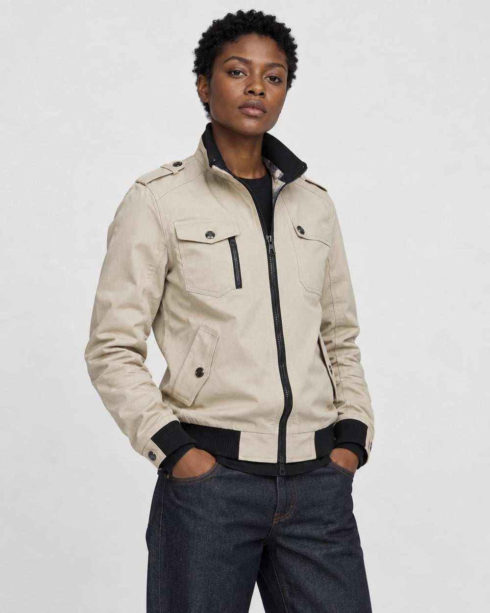 Model wearing the beige field jacket zipped over a black tee and dark jeans, three-quarter view