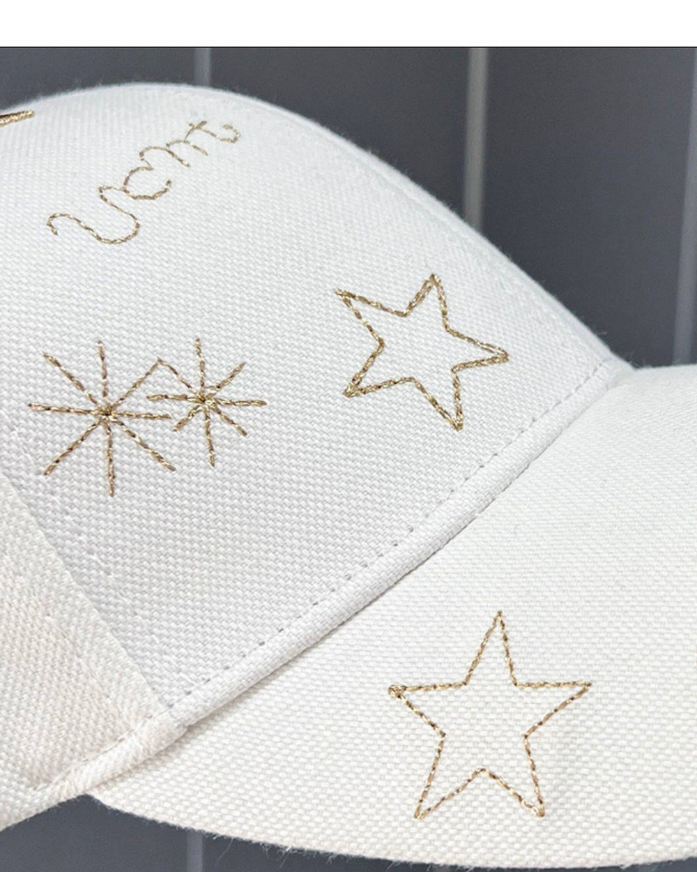 Close-up of gold outlined stars and spark symbols embroidered on the white cap