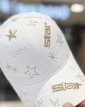 White baseball cap held in a hand, with gold star embroidery and the word star on the brim