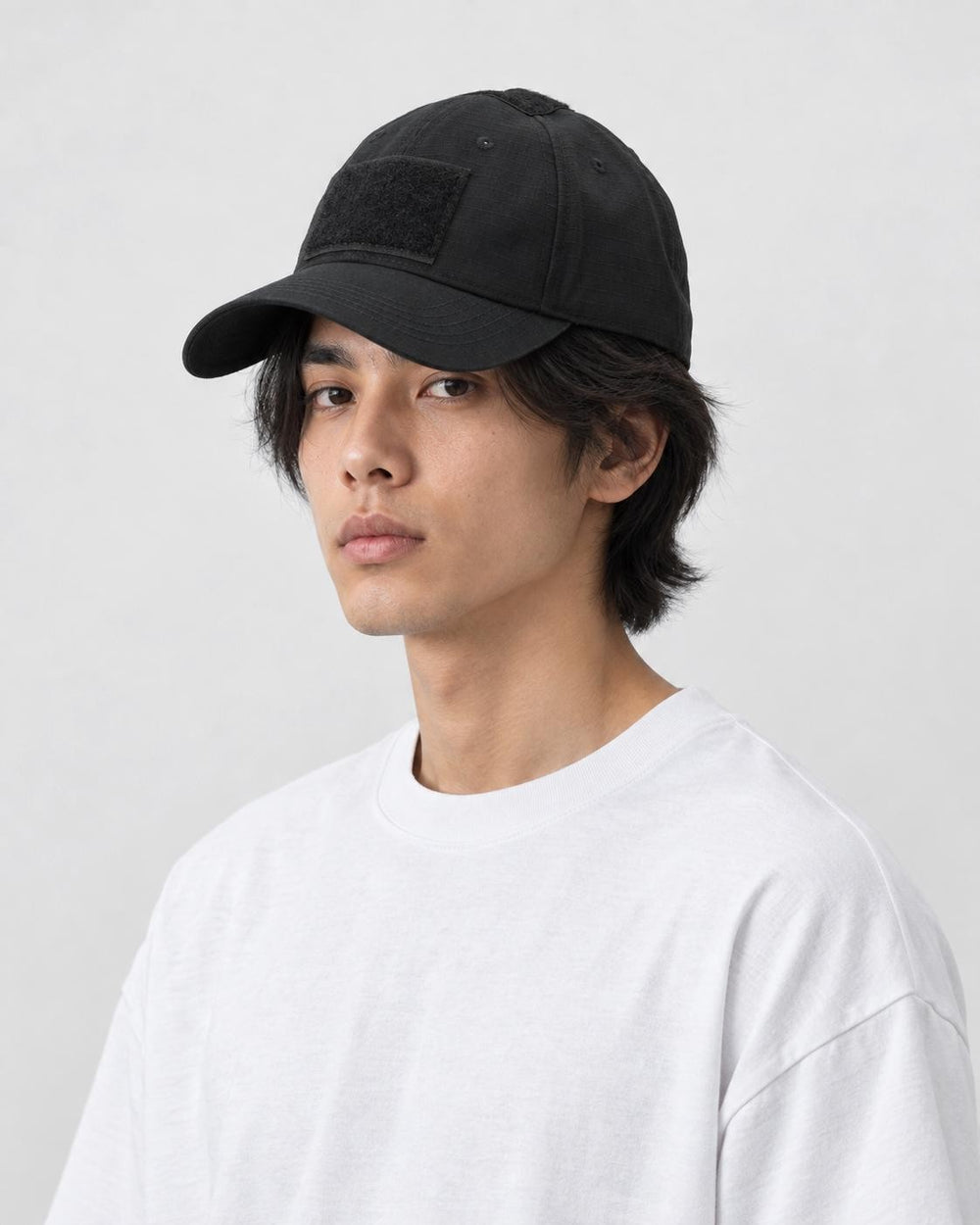 Man wearing the black tactical baseball cap with a white tee, three-quarter view