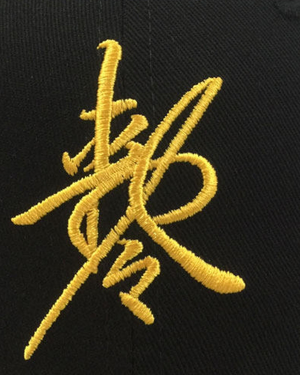 Close-up of the gold cursive talisman sign embroidered on black cotton