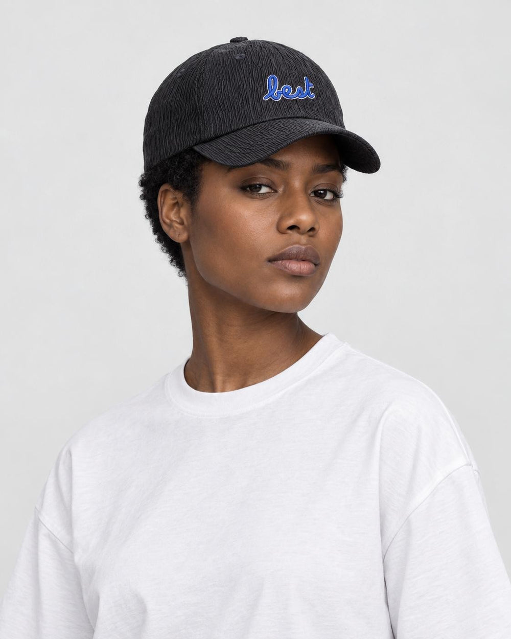 Woman wearing the black textured baseball cap with blue best embroidery and a white tee, three-quarter view