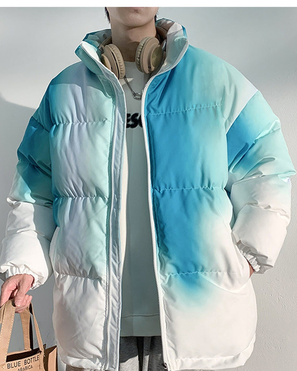 Blue-green tie-dye puffer jacket carried with a tote bag, torso view