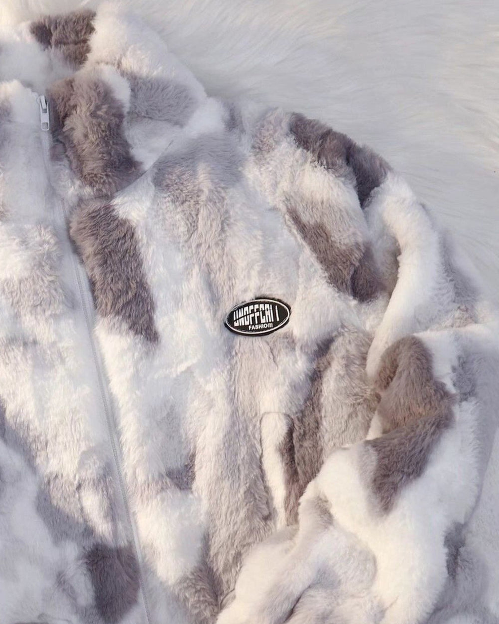 Close-up of the gray tie-dye plush pile, the white zip and the small oval patch on the chest