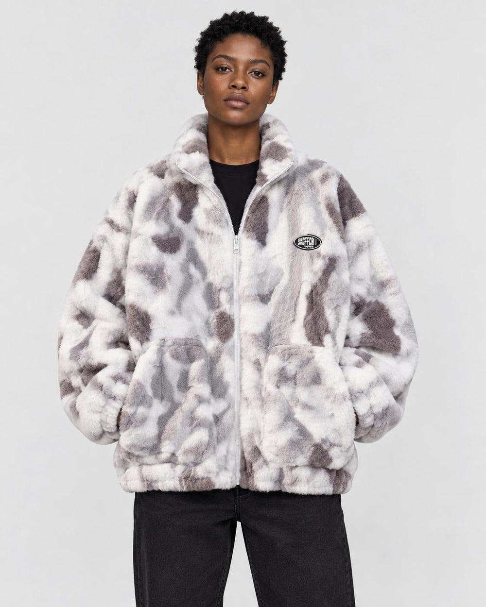 Model wearing the gray tie-dye plush zip jacket over a black tee and black jeans, front view