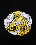 Close-up of the round white and gold swirl emblem embroidered on the chest