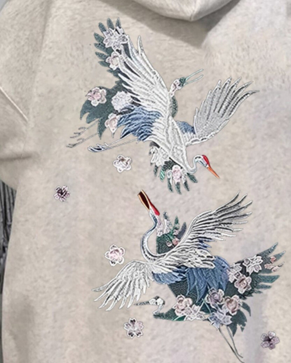 Close-up of the two embroidered cranes on the back of the oatmeal hoodie