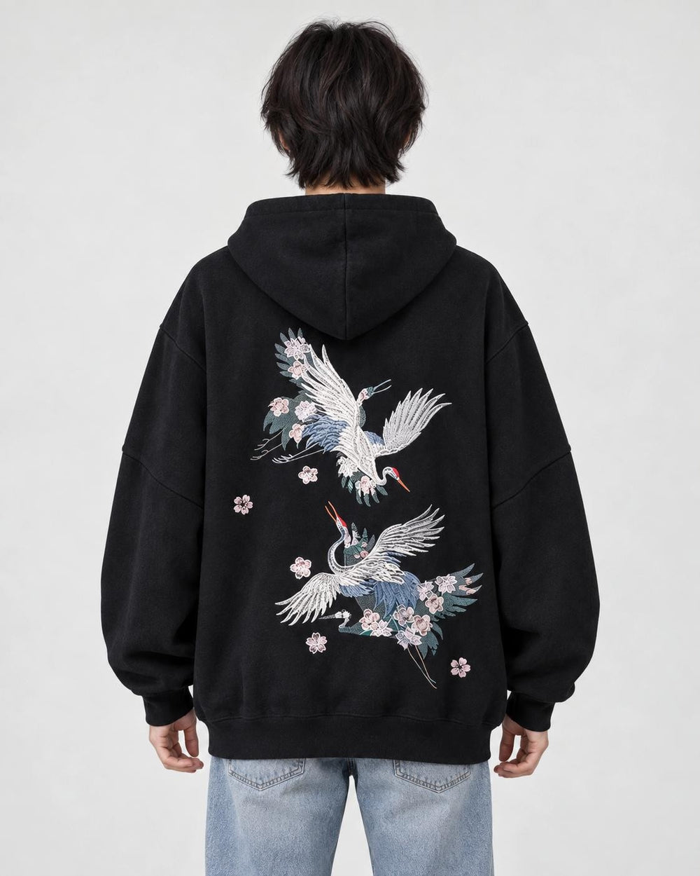 Model wearing the black crane embroidered hoodie with light-wash jeans, back view