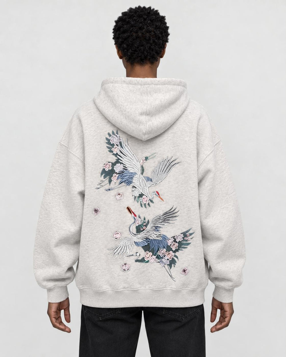 Model wearing the oatmeal crane embroidered hoodie with black jeans, back view