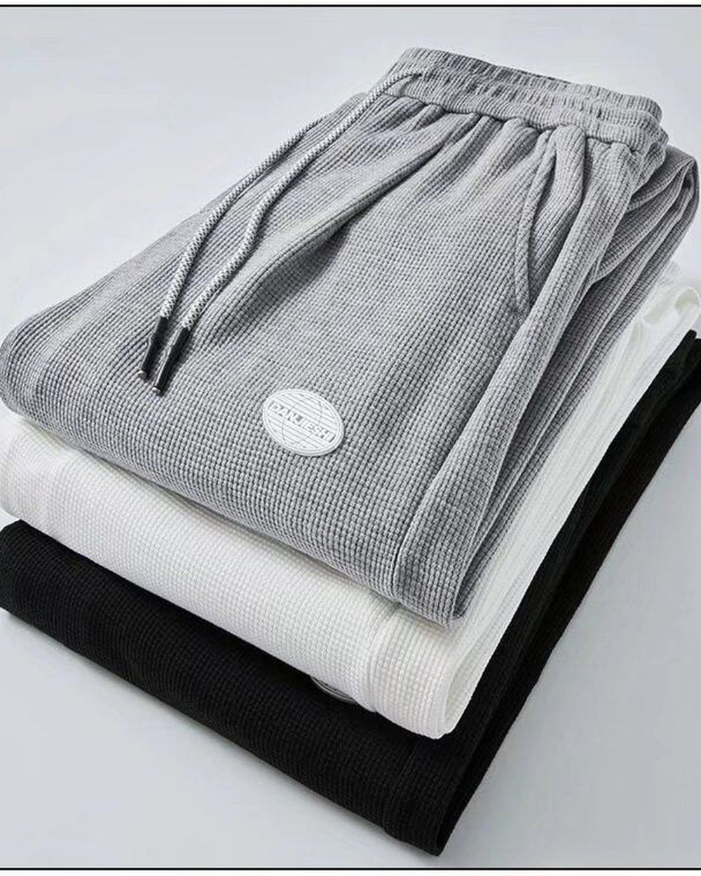 Folded gray, white and black waffle knit joggers showing the drawcord and patch label