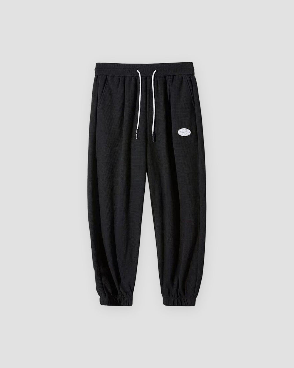 Black waffle knit joggers with a white drawcord and ribbed ankle cuffs, front view