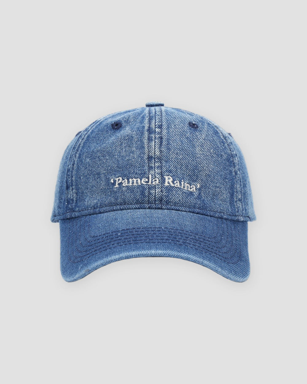 Front view of the dark blue denim cap with white Pamela Raina lettering and eyelets