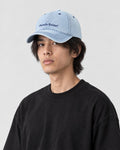 Man wearing the light blue denim baseball cap with Pamela Raina lettering, three-quarter view