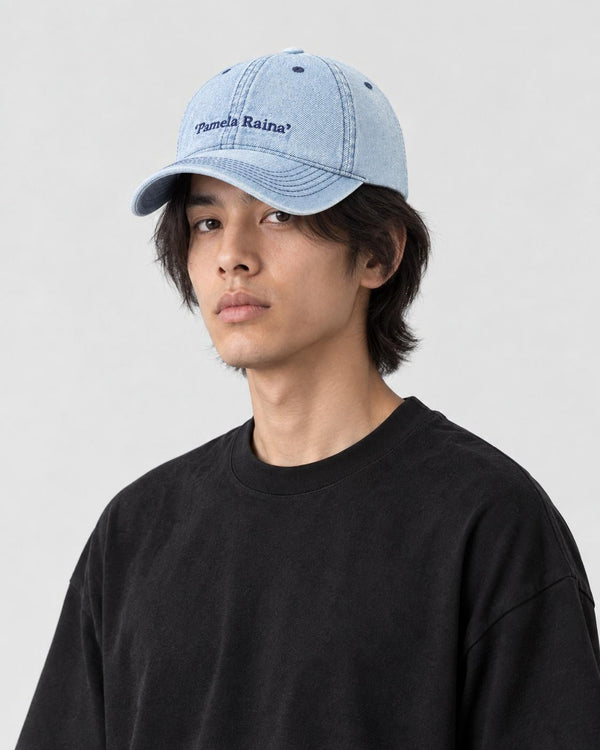Man wearing the light blue denim baseball cap with Pamela Raina lettering, three-quarter view
