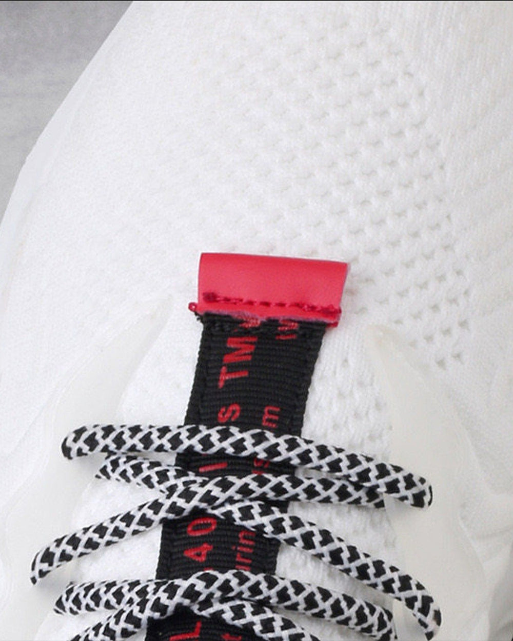 Close-up of the white knit, red pull tab and speckled round laces