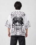 Man seen from behind in the white haori printed with a black line-art demon mask and peonies, over a black tee
