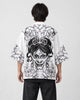 Man seen from behind in the white haori printed with a black line-art demon mask and peonies, over a black tee