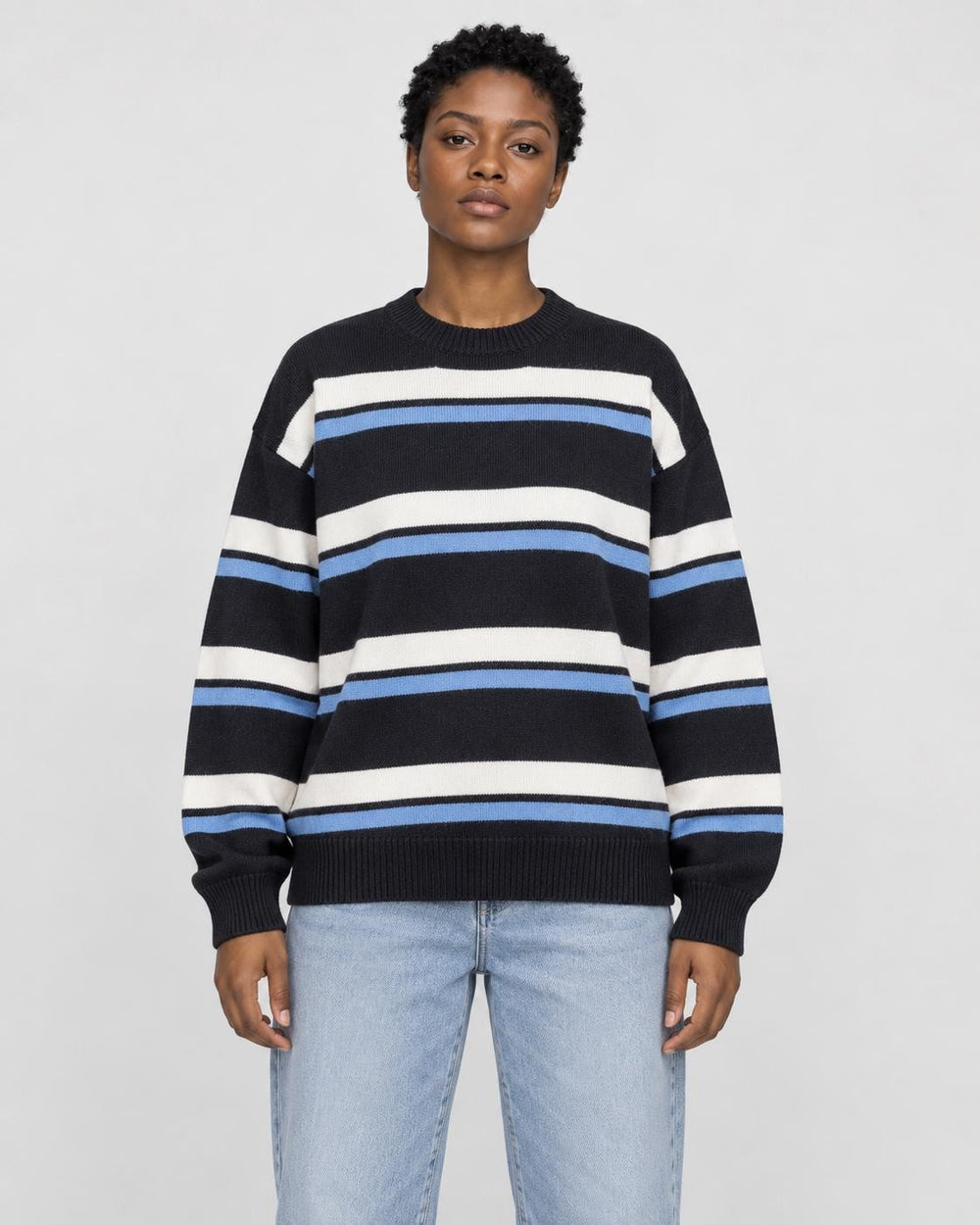 Model wearing the black striped knit sweater with light-wash jeans, front view