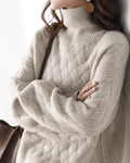Woman in a loose beige basket-weave knit sweater with a ribbed mock neck, arms crossed and a brown tote on her shoulder