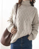 Woman in the beige woven sweater with a brown shoulder bag, the ribbed cuff resting at her jeans pocket