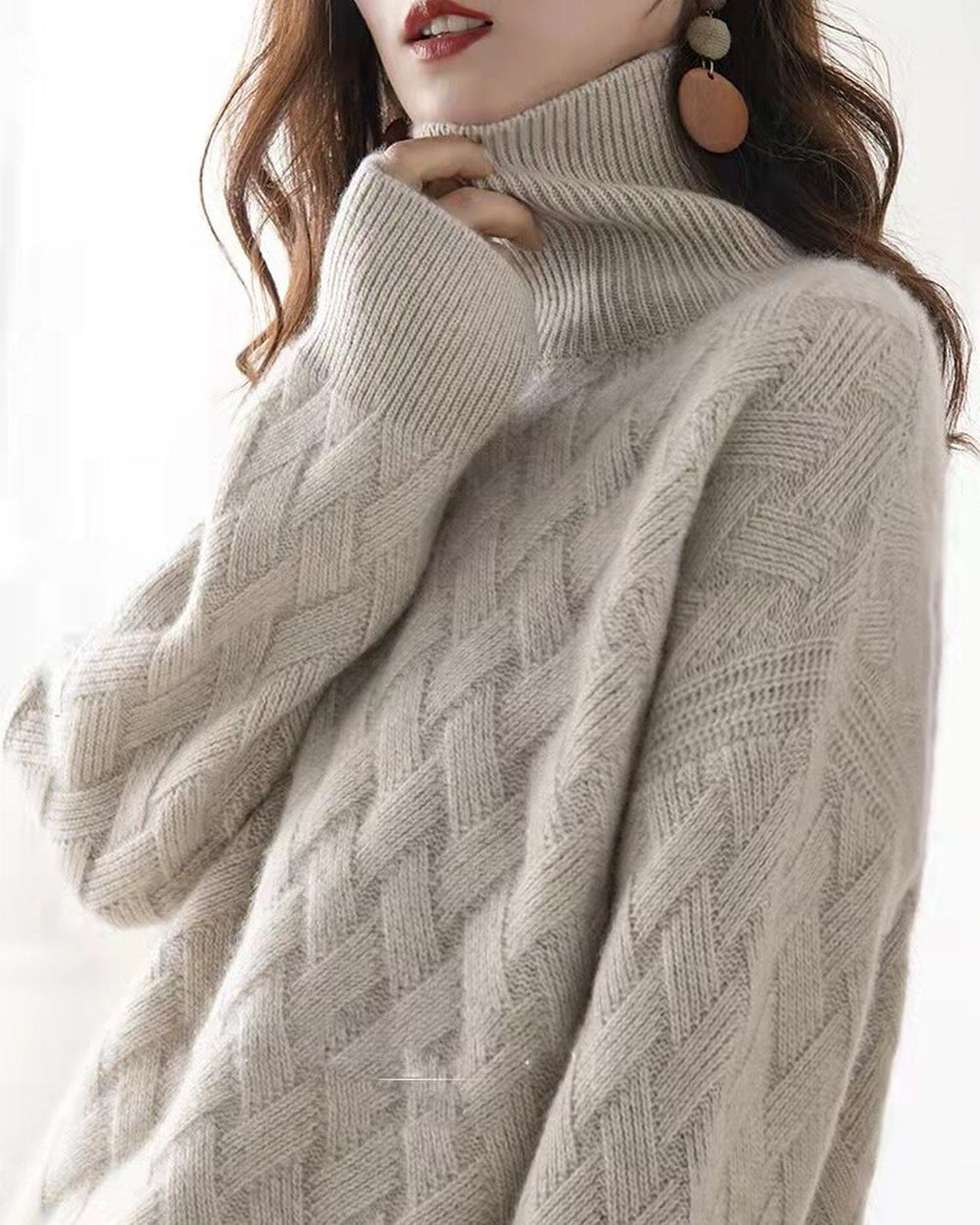 Beige woven-knit sweater with a ribbed mock neck, one hand raised to the collar and the wide sleeve falling loose