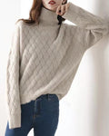 Woman leaning on a white wall in the beige woven sweater, one arm raised, the knit texture visible on the sleeve