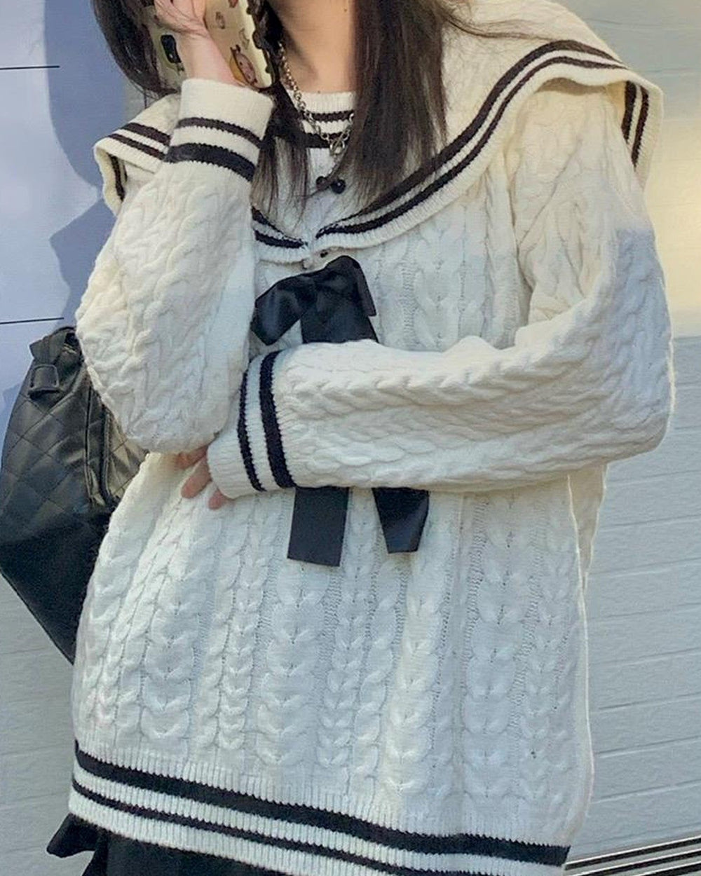 Side view of the cream cable-knit sweater with the striped collar, bow and hem band
