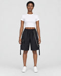 Woman in black knee-length cargo shorts with a silver chain and side straps, a white cropped tee and white sneakers