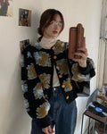 Black flower-patch jacket worn over a lace top and jeans, photographed against a white wall
