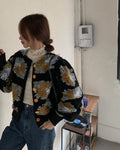 Woman in the black flower-patch jacket with a hand raised to take a photo