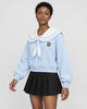 Woman in a light blue sailor-collar sweatshirt with an ivory collar and tie over a black pleated skirt, turned slightly