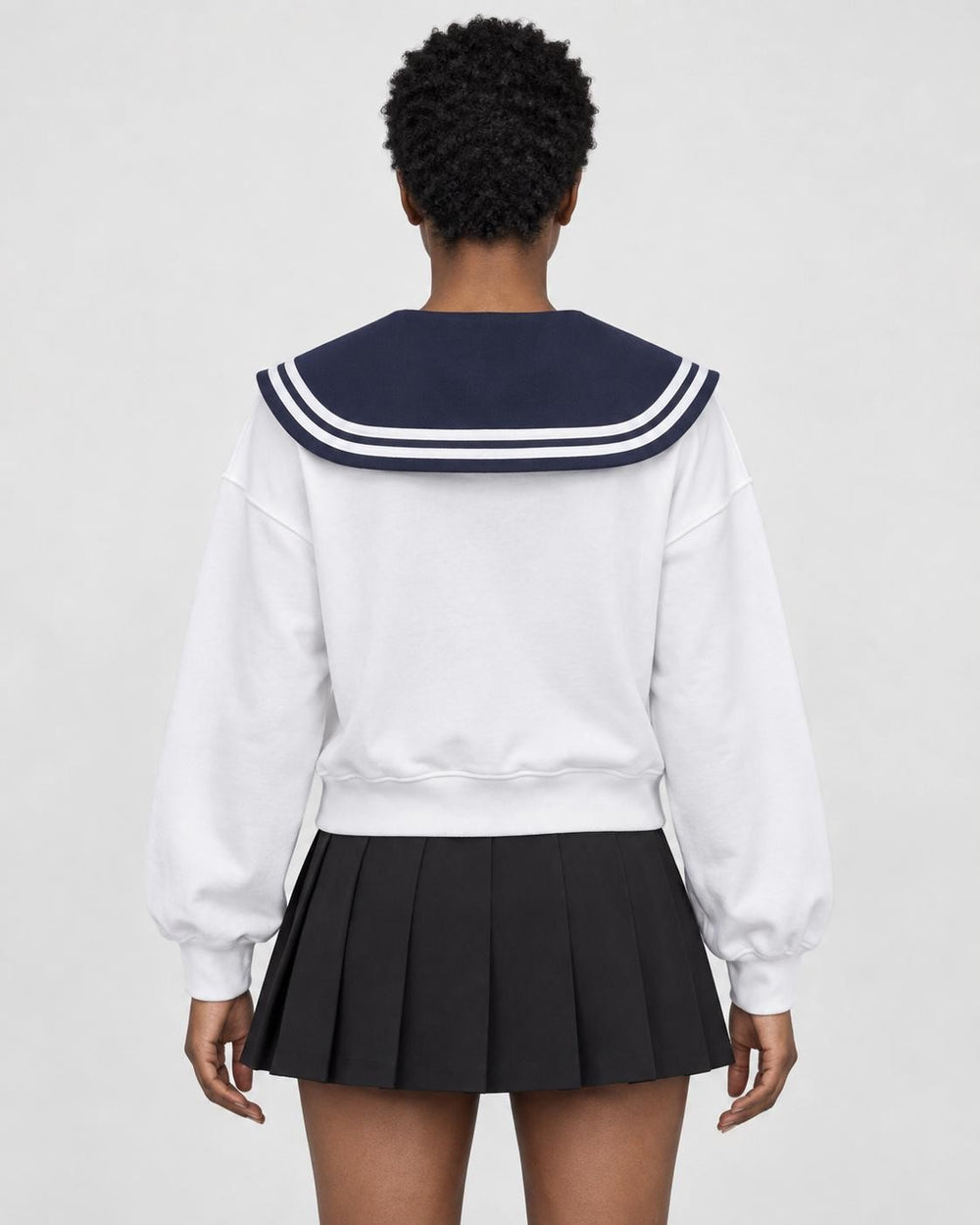 Woman seen from behind in the white sweatshirt with the large navy sailor collar over a black pleated skirt