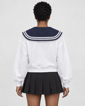 Woman seen from behind in the white sweatshirt with the large navy sailor collar over a black pleated skirt
